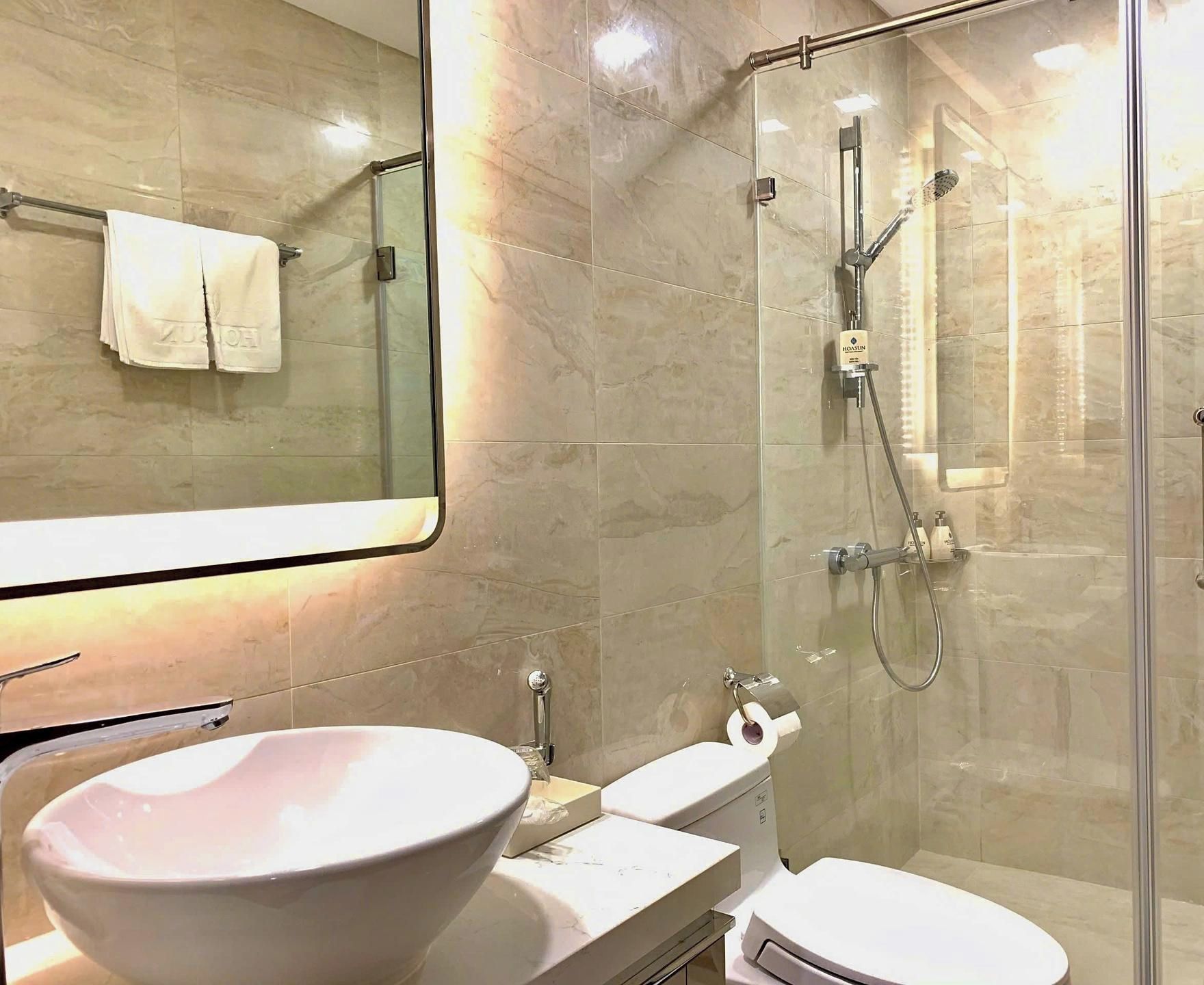 Un baño moderno con un espejo grande, cabina de ducha con cristal, lavabo blanco y un inodoro.