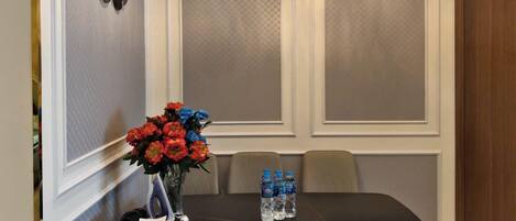 A dining area with a table, chairs, a vase of flowers, and a wall clock.