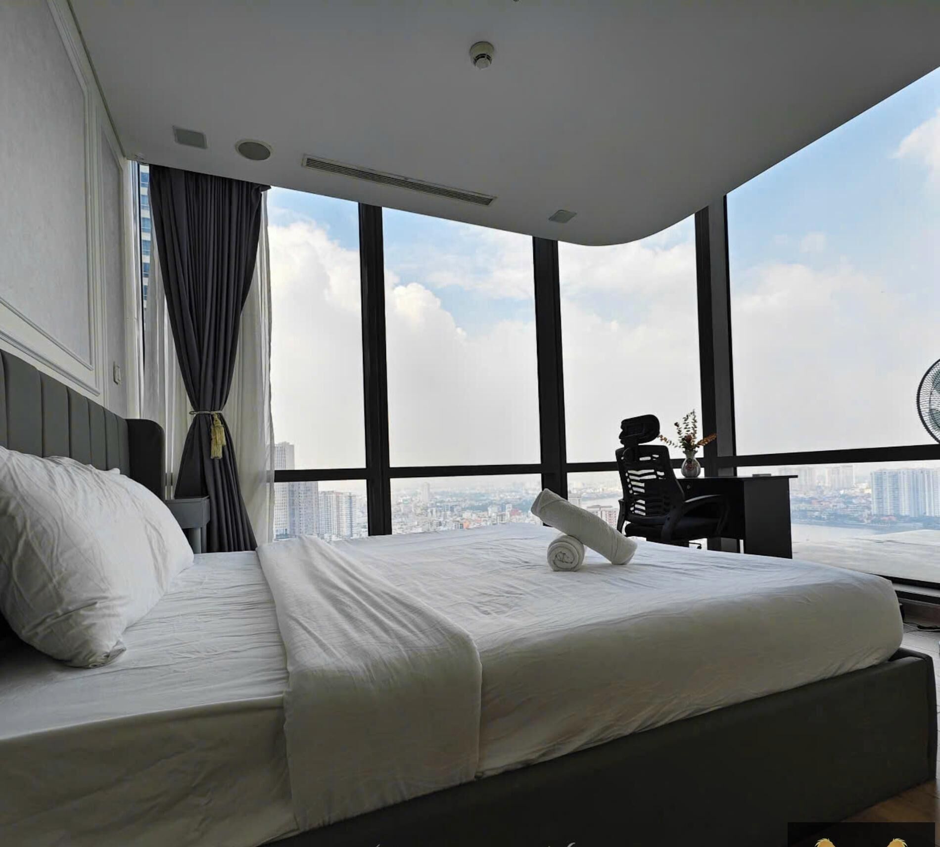 A modern hotel room with a large bed, a desk, and a city view through large windows.