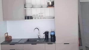 Een moderne keuken met een inbouwfornuis, spoelbak en bovenkasten. Er is een zithoek met een tafel en stoelen, en een bank.