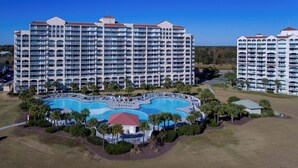 A large hotel with multiple balconies and a central swimming pool surrounded by palm trees.