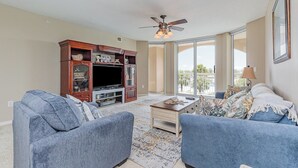 A living room with a television, two blue armchairs, a coffee table, and a ceiling fan.