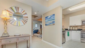 A kitchen with white cabinets, a microwave, and a stove. There is a dining table with a lamp and a mirror on the wall.