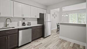 A modern kitchen with white cabinets, stainless steel appliances, and a wooden floor.