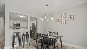 A modern kitchen with stainless steel appliances, a dining area with a wooden table and chairs, and a chandelier with multiple bulbs.
