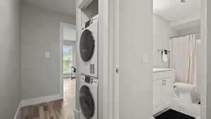 A laundry room with a front-loading washer and dryer, a toilet, and a shower area.