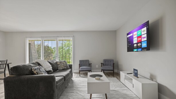 A modern living room with a gray sofa, two armchairs, a coffee table, and a flat-screen TV mounted on the wall displaying streaming services.