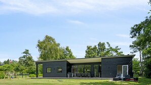 Ett modernt hus i två våningar med en stor entré bestående av en glasdörr, en täckt uteplats och en välskött gräsmatta.