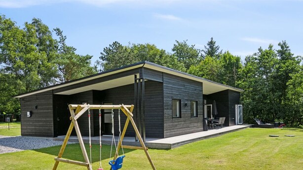 Ett modernt hus med en täckt uteplats, en gunga och en välskött gräsmatta.