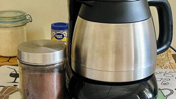 A coffee maker, a jar of coffee, and a container of creamer on a table with a coffee-themed placemat.