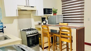 A compact kitchen with a gas stove, oven, microwave, and a small dining area with wooden chairs. - Cozy apartment in phenomenal Managua with WiFi, AC, garache and kitchen. (Managua)