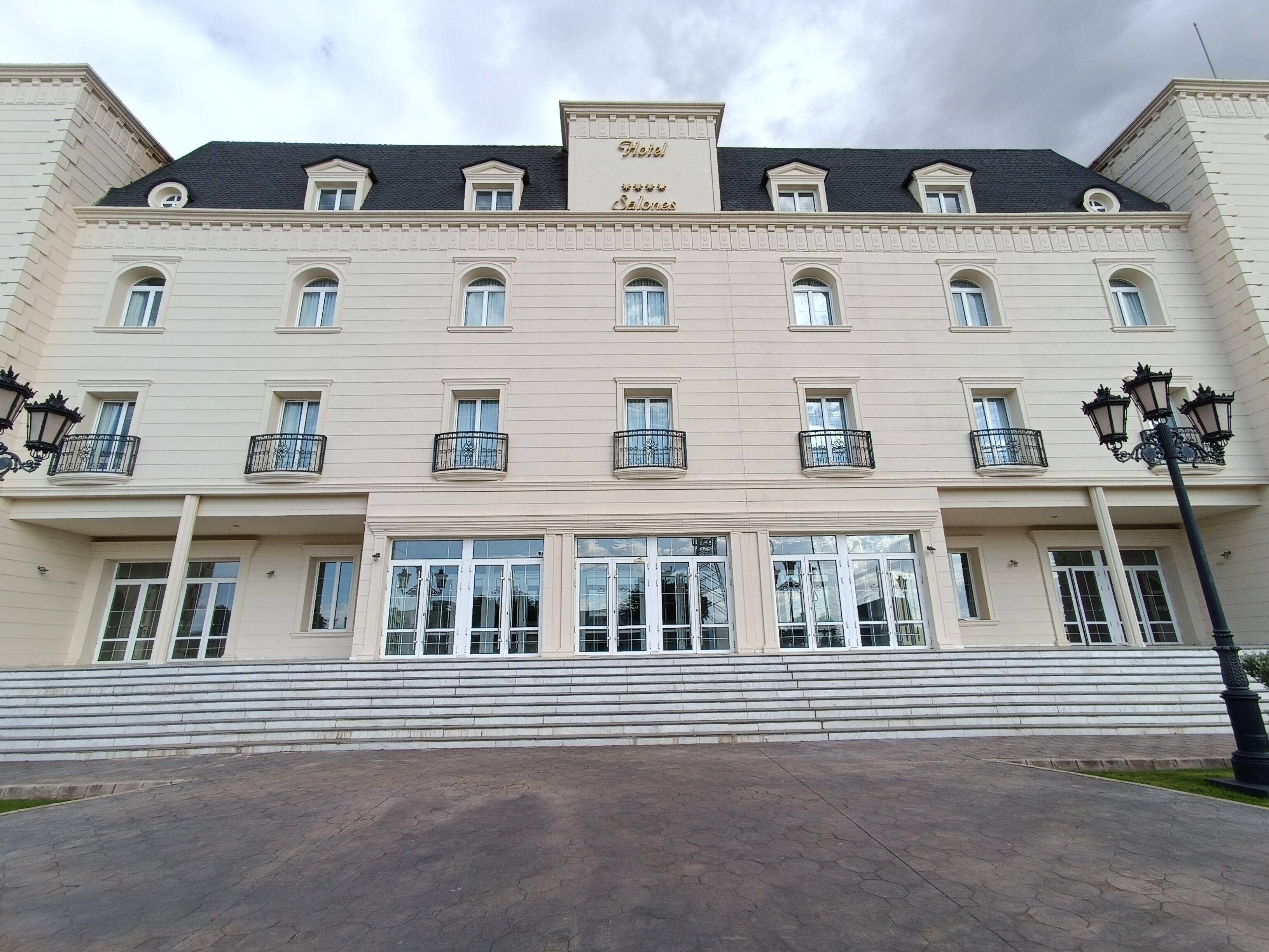 Un hotel grande de varios pisos con un estilo arquitectónico clásico, que presenta una entrada central con escalones que conducen a un par de puertas dobles.