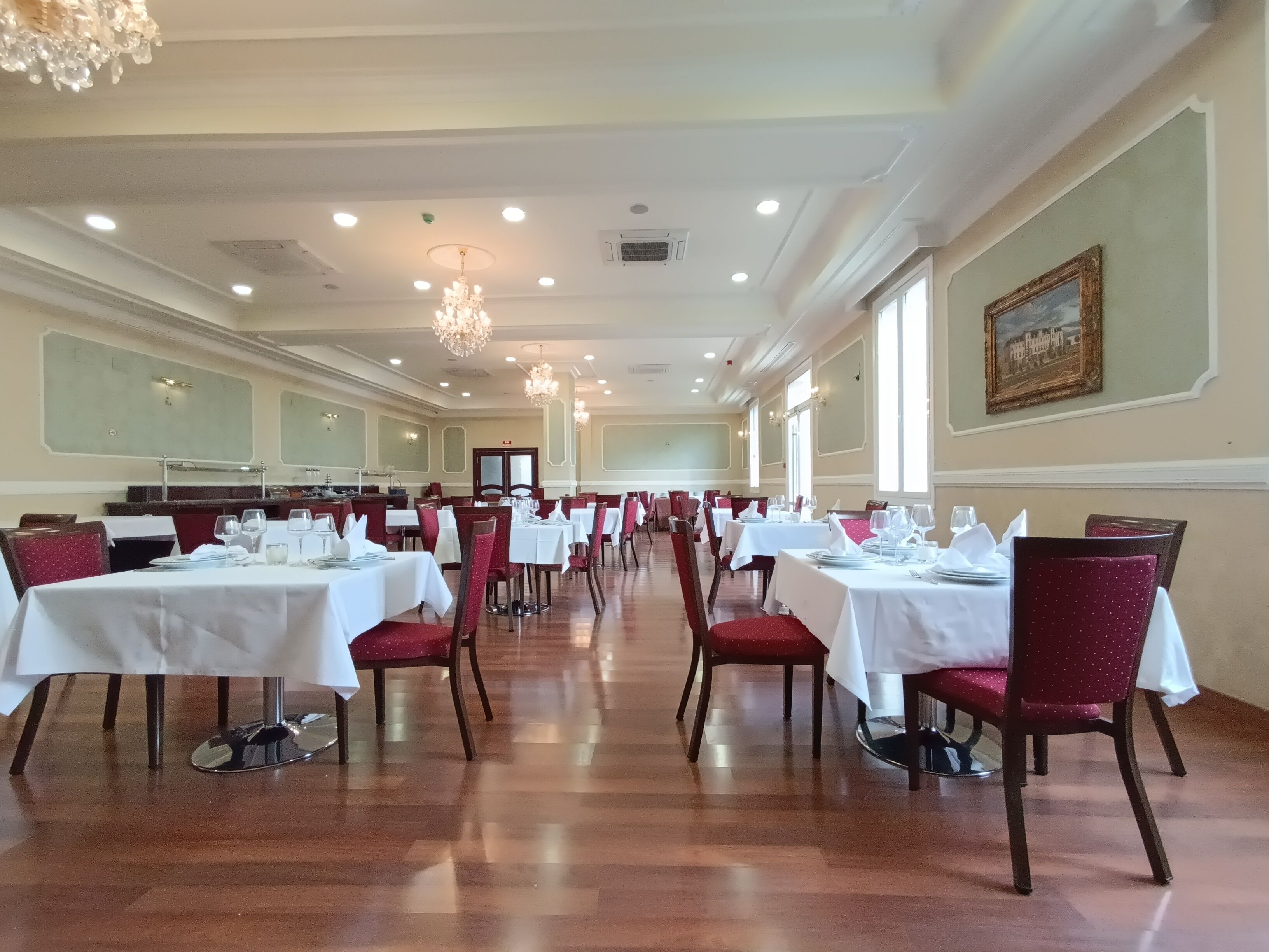 A spacious dining hall with rows of tables and chairs, large windows, and chandeliers.