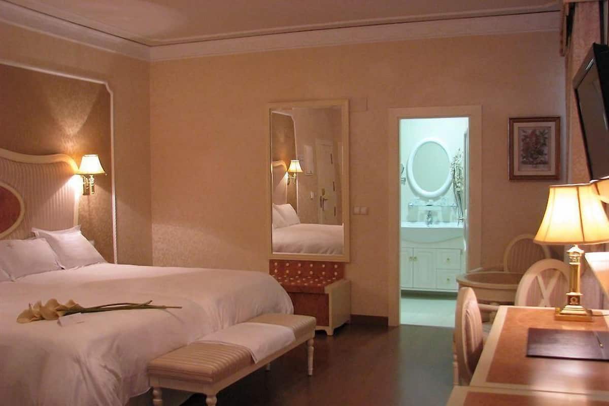 Een hotelkamer met een groot bed, een bankje, een bureau en een spiegel.