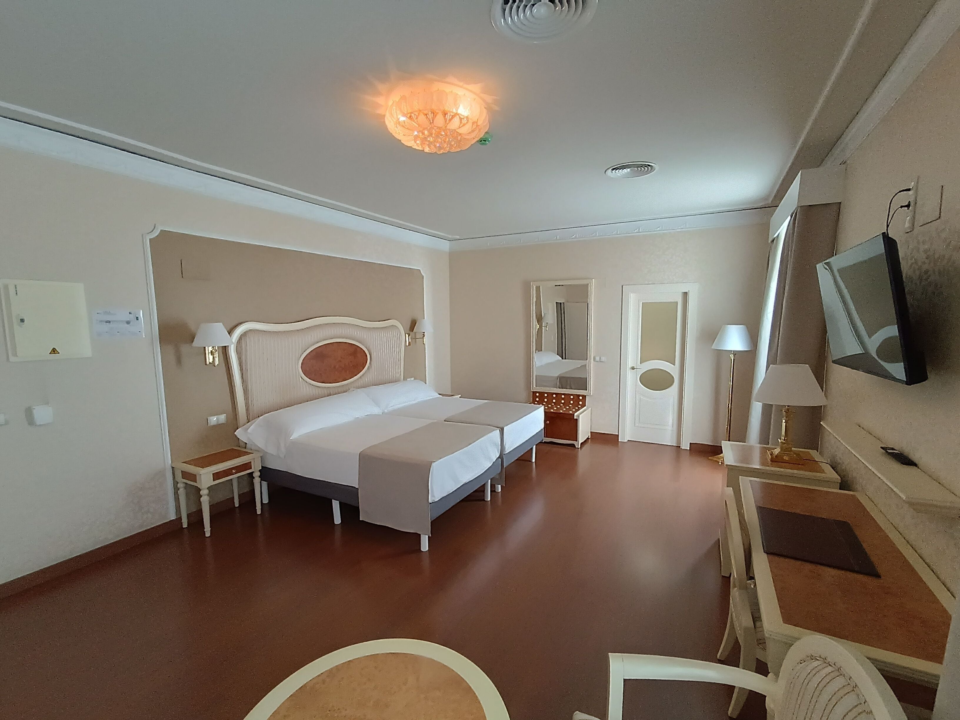 A hotel room with a bed, bedside tables, a TV, and a desk with a chair.