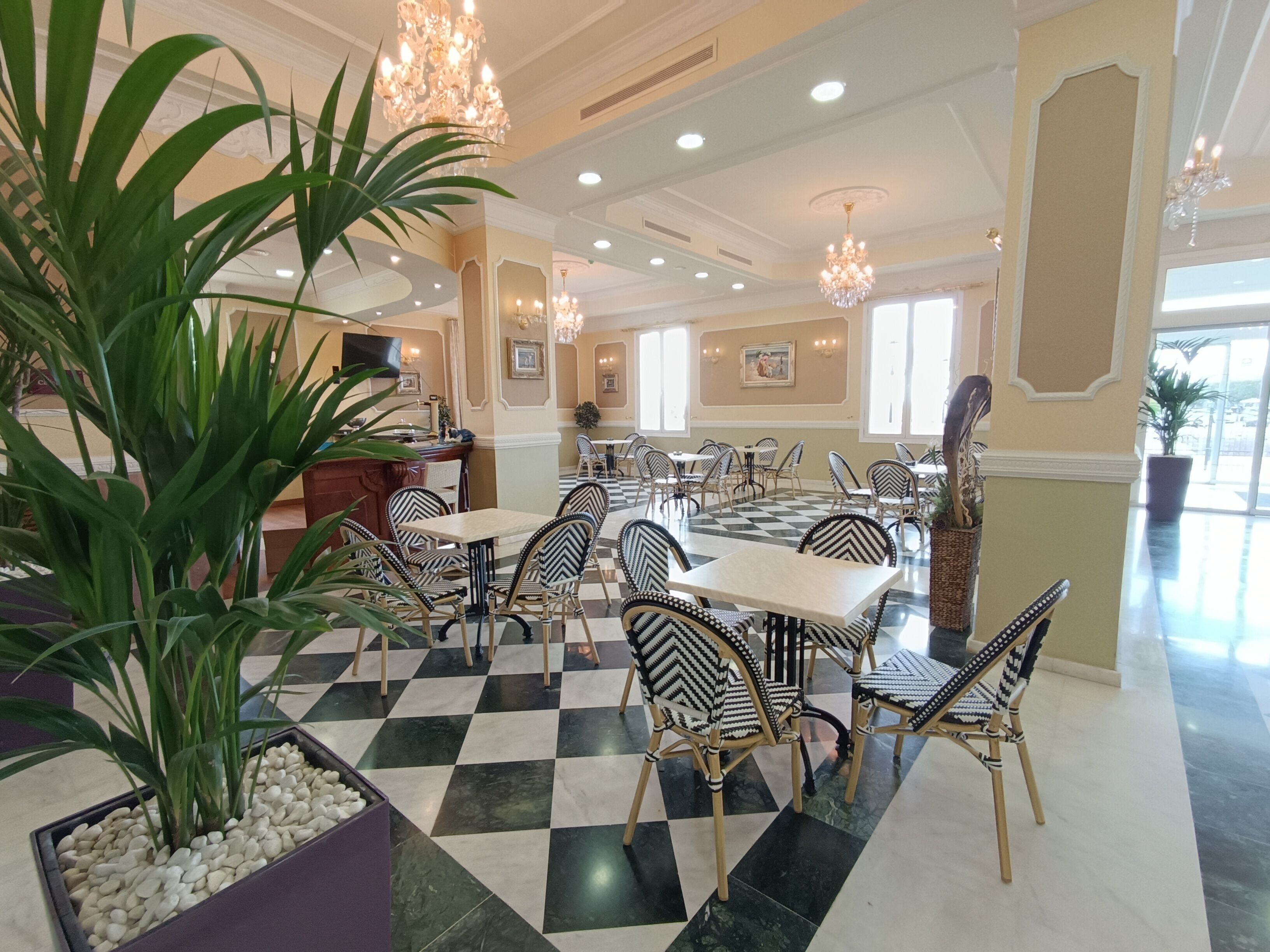 A hotel lobby with checkered flooring, wicker furniture, and a large potted plant.