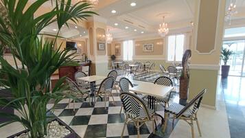 A hotel lobby with checkered flooring, wicker furniture, and a large potted plant.