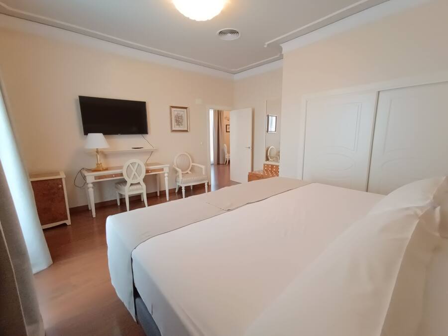 Habitación de hotel con una cama grande, un escritorio con silla, televisión y una puerta que da a otra habitación.