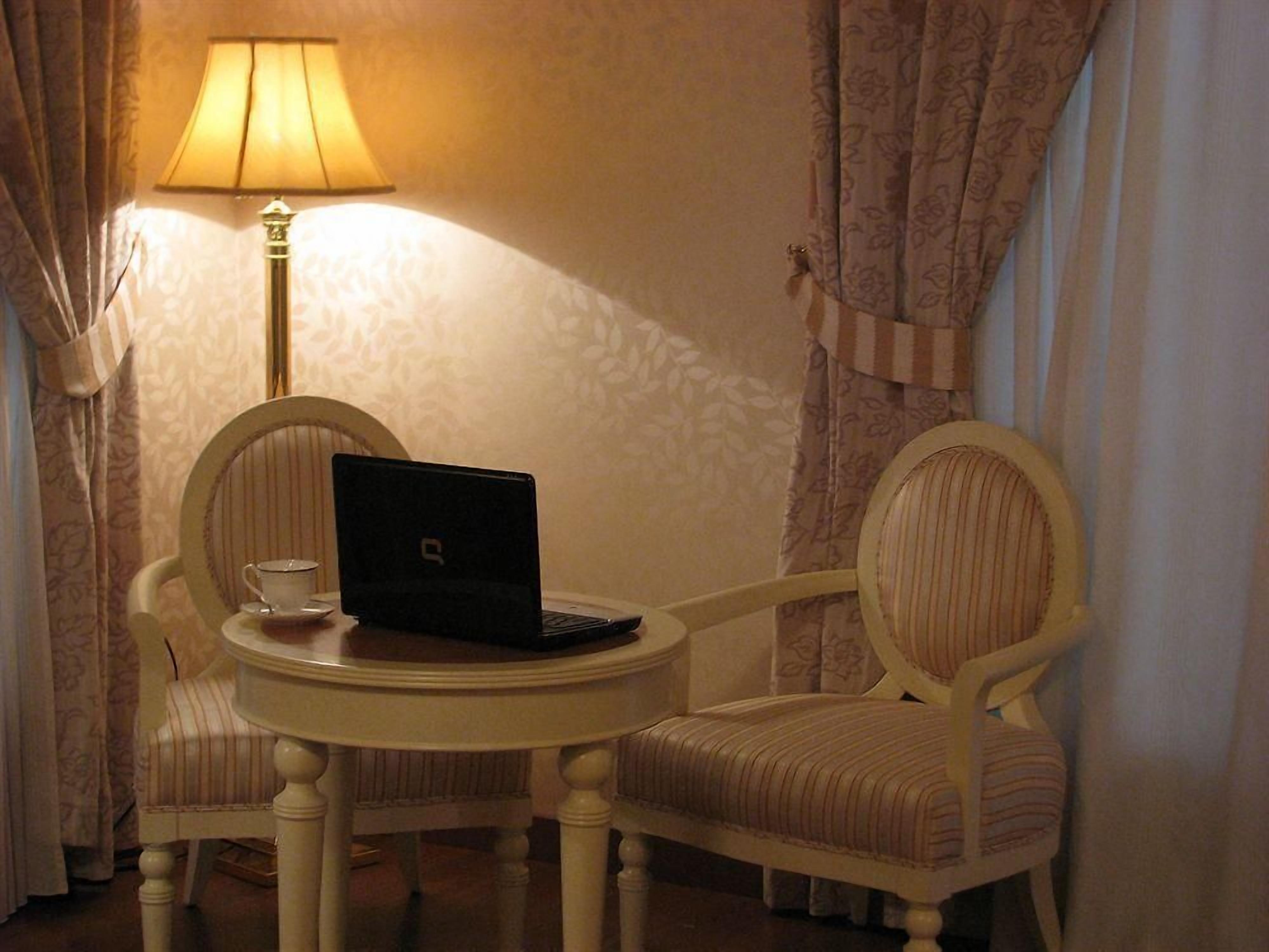A small round table with a laptop and a cup, two upholstered chairs, a lamp, and curtains.