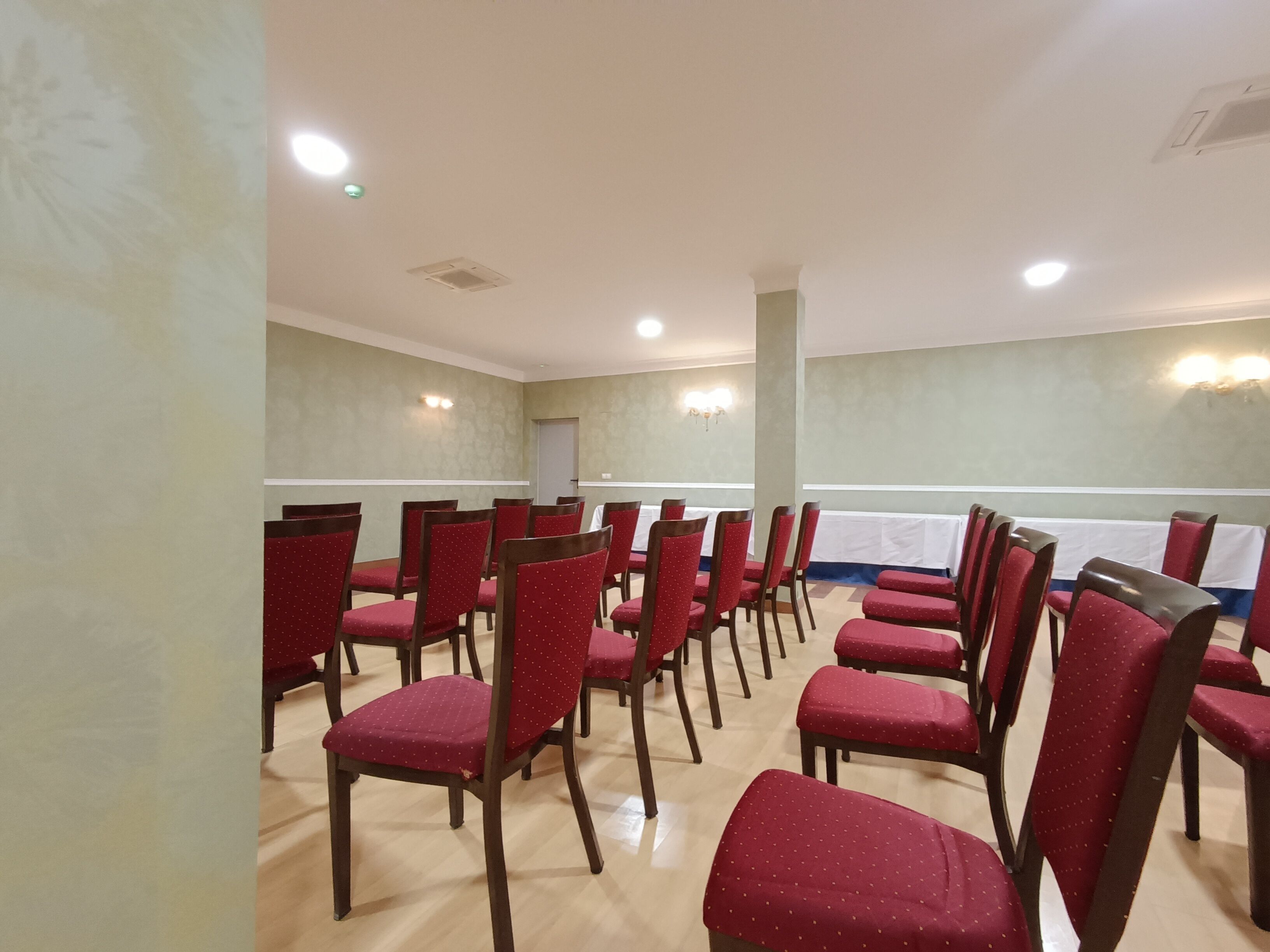 A conference room with rows of red chairs, a white tablecloth-covered table, and wall-mounted lighting.