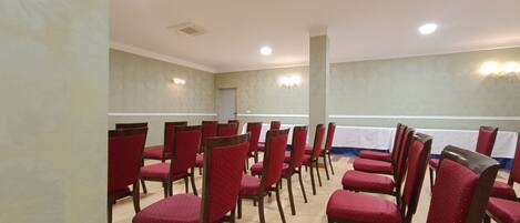 A conference room with rows of red chairs, a white tablecloth-covered table, and wall-mounted lighting.