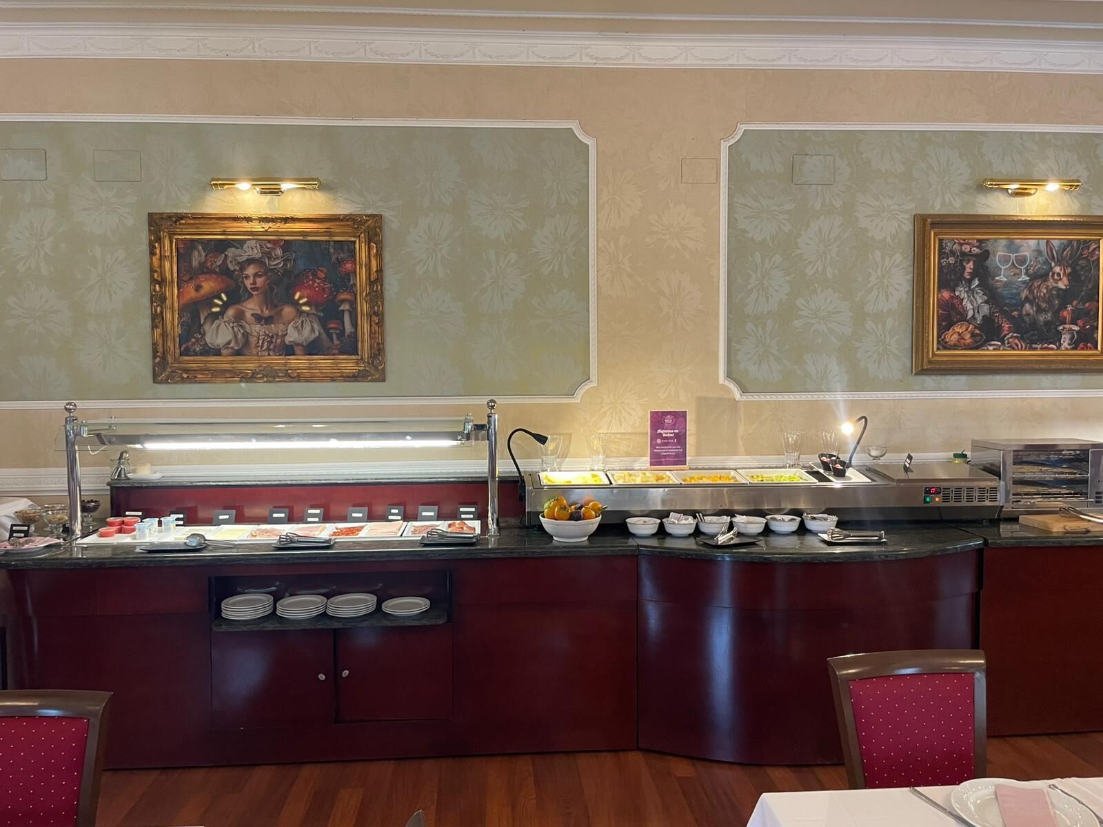 Un buffet proposant divers plats et une machine à café. Deux tableaux encadrés sont accrochés au mur, au-dessus du buffet.