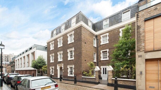 A row of modern brick townhouses with uniform windows, a paved street, and parked cars.