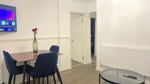 A dining area with a table, chairs, a vase with flowers, and a TV mounted on the wall.