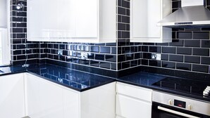A modern kitchen with white cabinets, black tiled backsplash, and a black countertop.