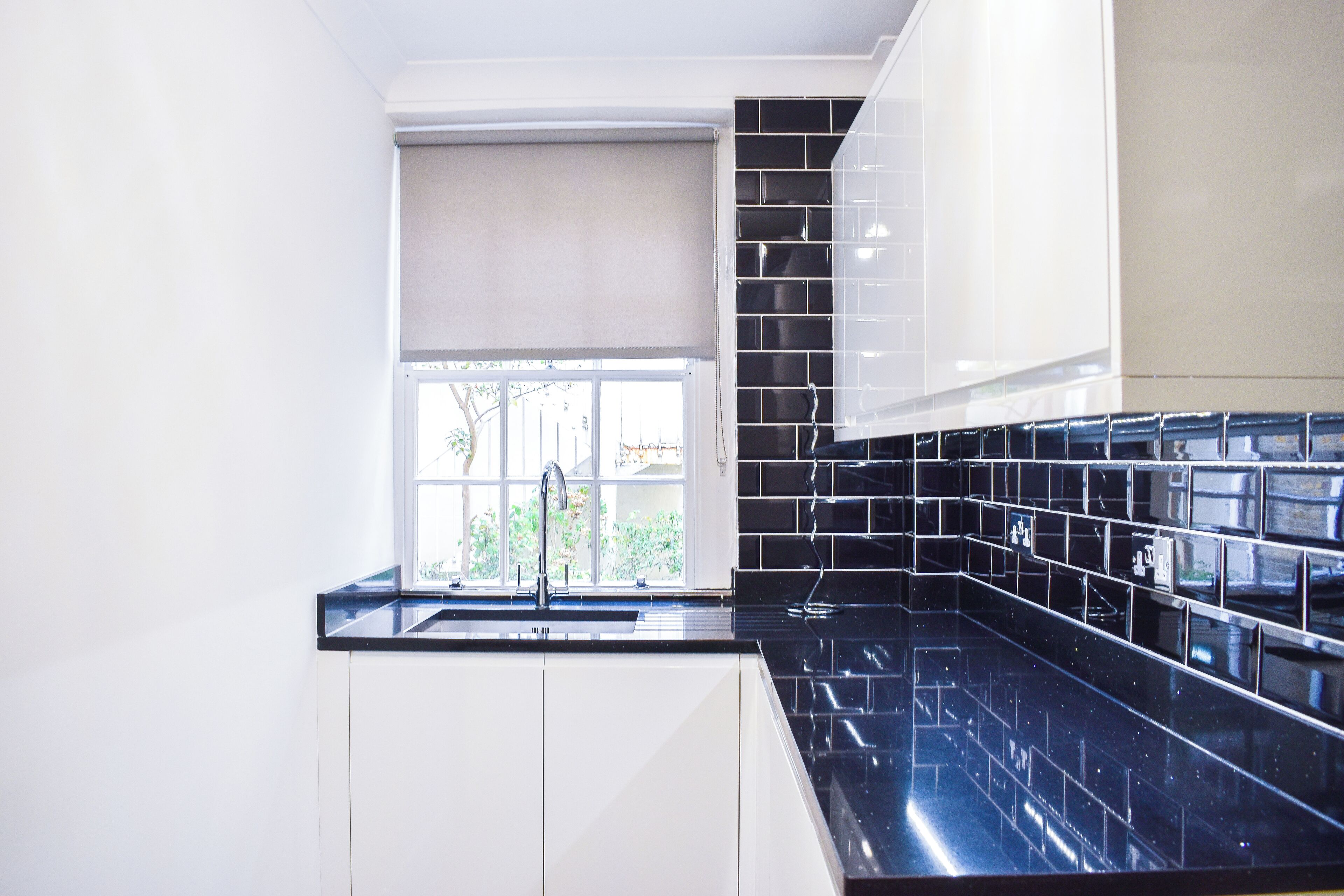 A modern kitchen with white cabinets, a black countertop, and a window with a view of greenery.
