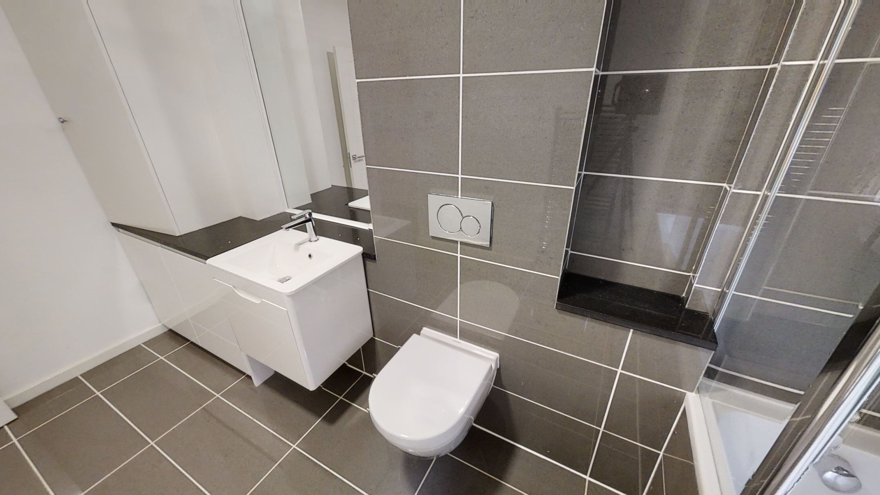 Ett badrum med en vit toalett, ett vitt handfat och en duschhörna.