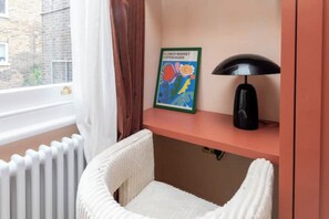 A room with a white radiator, a white chair, a pink shelf with a flower market sign, and a black lamp.