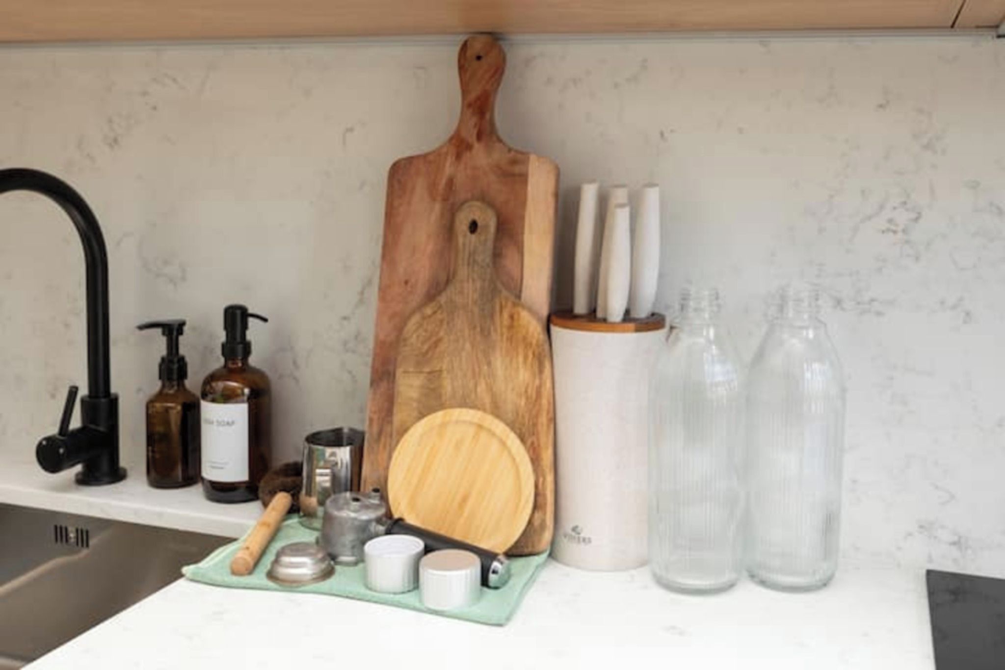 Een keukenblad met een houten snijplank, een messenblok, een zeepdispenser en een fles afwasmiddel.
