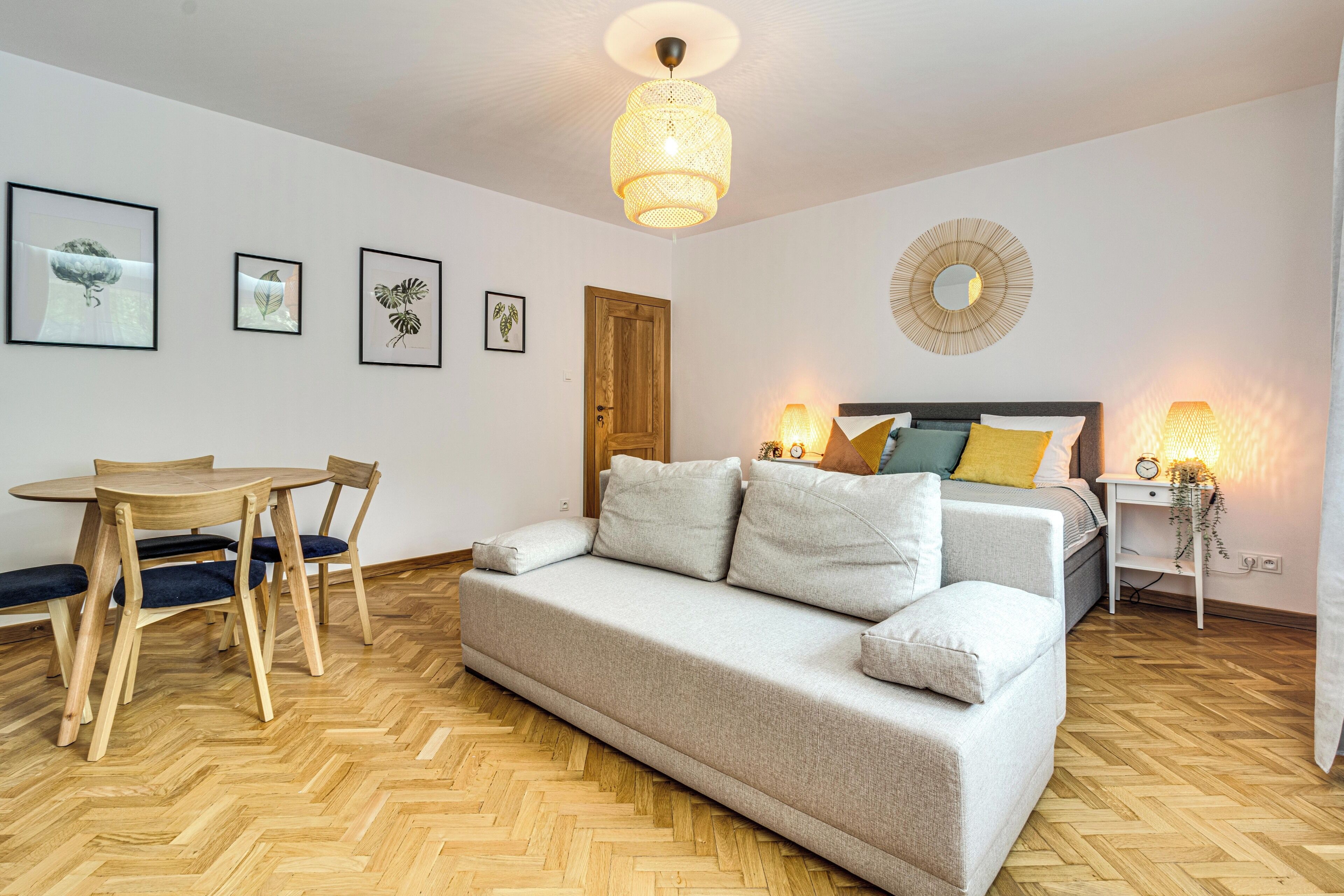 Una habitación moderna con sofá, una mesa de comedor con sillas, una cama con cabecero y una obra de arte colgada en la pared.