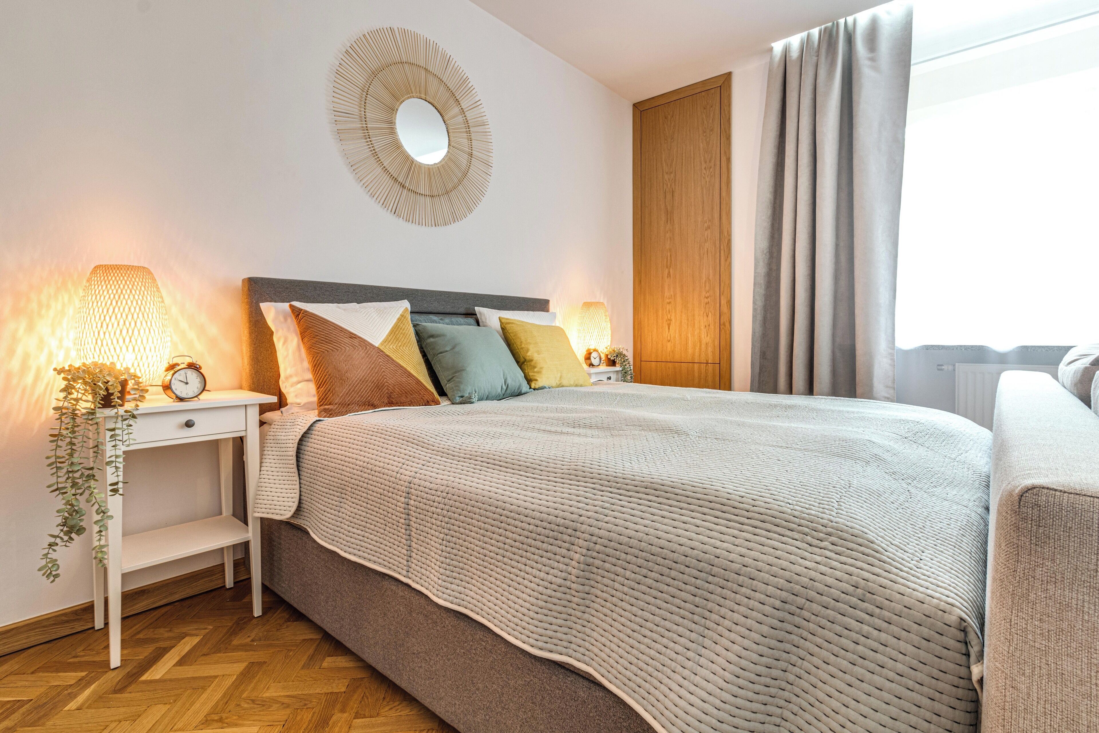 Ein ordentlich eingerichtetes Schlafzimmer mit Bett, Nachttischen, einem Spiegel und einem Fenster mit Vorhängen.
