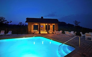 Ein Pool mit einer Liegeinsel, ein Gebäude mit überdachter Terrasse und Liegestühlen.