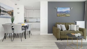 A modern living room with a grey sofa, a dining area with a table and chairs, and a kitchen in the background.