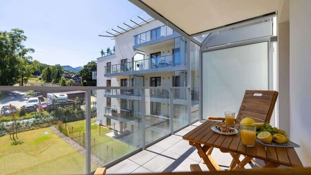A balcony with a table set for breakfast, overlooking a residential area and a parking lot.