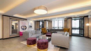 A modern hotel lobby with a grey sofa, two round ottomans, a coffee table, and a large poster on the wall.