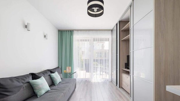 A modern living room with a grey sofa, a small side table, and a view through a large window to the outside.