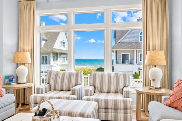A room with a view of the ocean, featuring striped armchairs, a sofa, and two lamps. - Our Happy Place #170 Ocean & Sound Views, Hot Tub, Pool & Beach Access (North Topsail Beach)