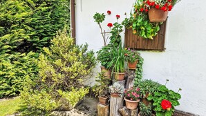 Ein Garten mit verschiedenen Blumentöpfen und Blumen, einer hölzernen Bank und einer weißen Mauer.