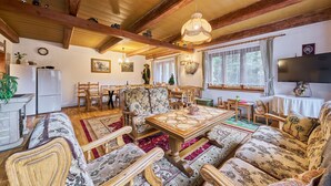 Ein gemütliches Wohnzimmer mit Holzbalken, einem Essbereich mit gemusterten Stühlen und einem großen Fernseher an der Wand.