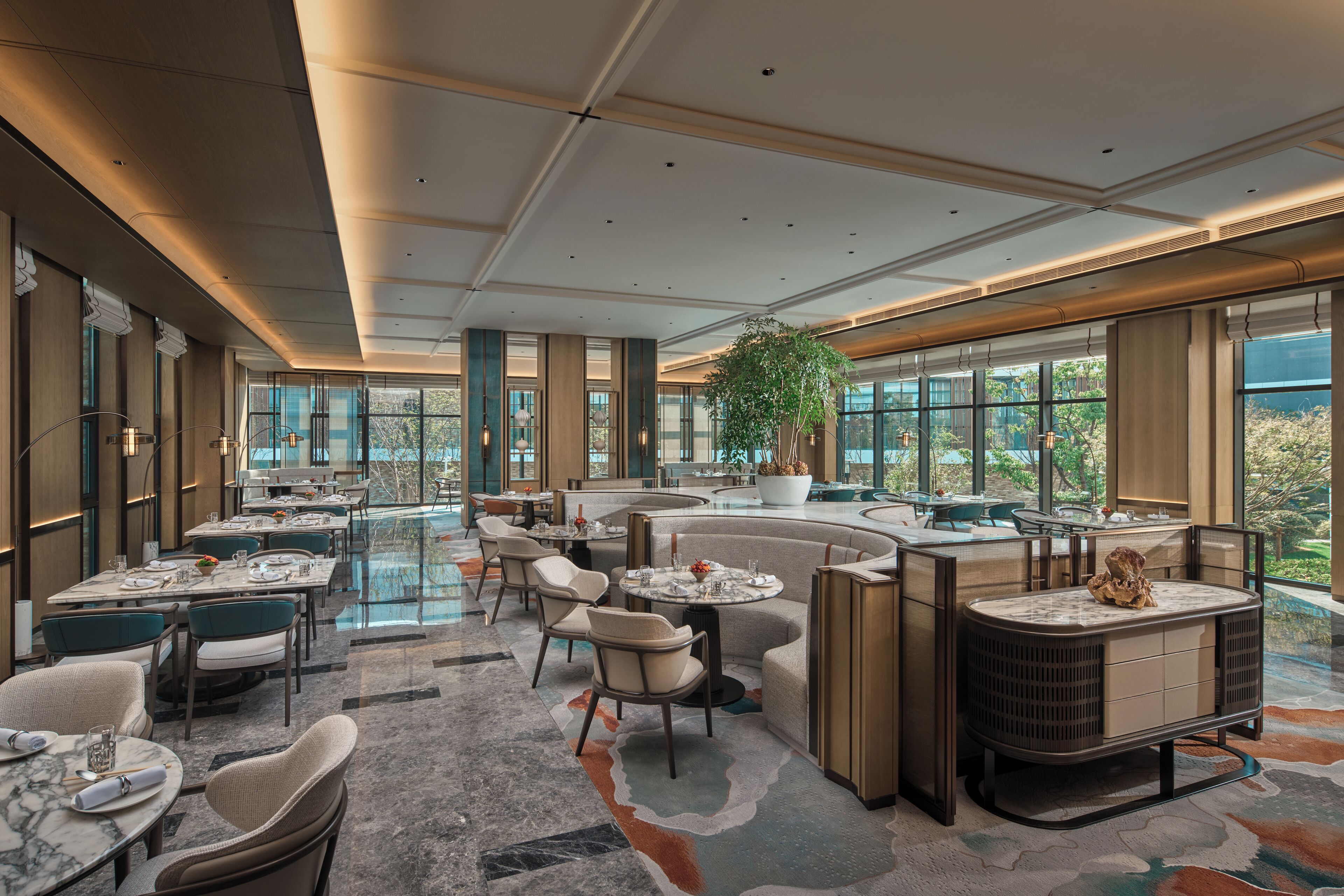 Un hall d’hôtel spacieux avec un espace salon central, de grandes fenêtres donnant sur l’extérieur et un aménagement intérieur moderne.