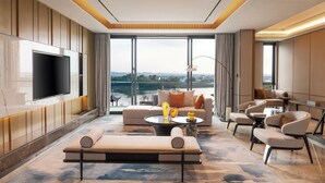Ett modernt hotellrum med en stor TV, bekväma sittmöbler, utsikt över staden och ett stort fönster.