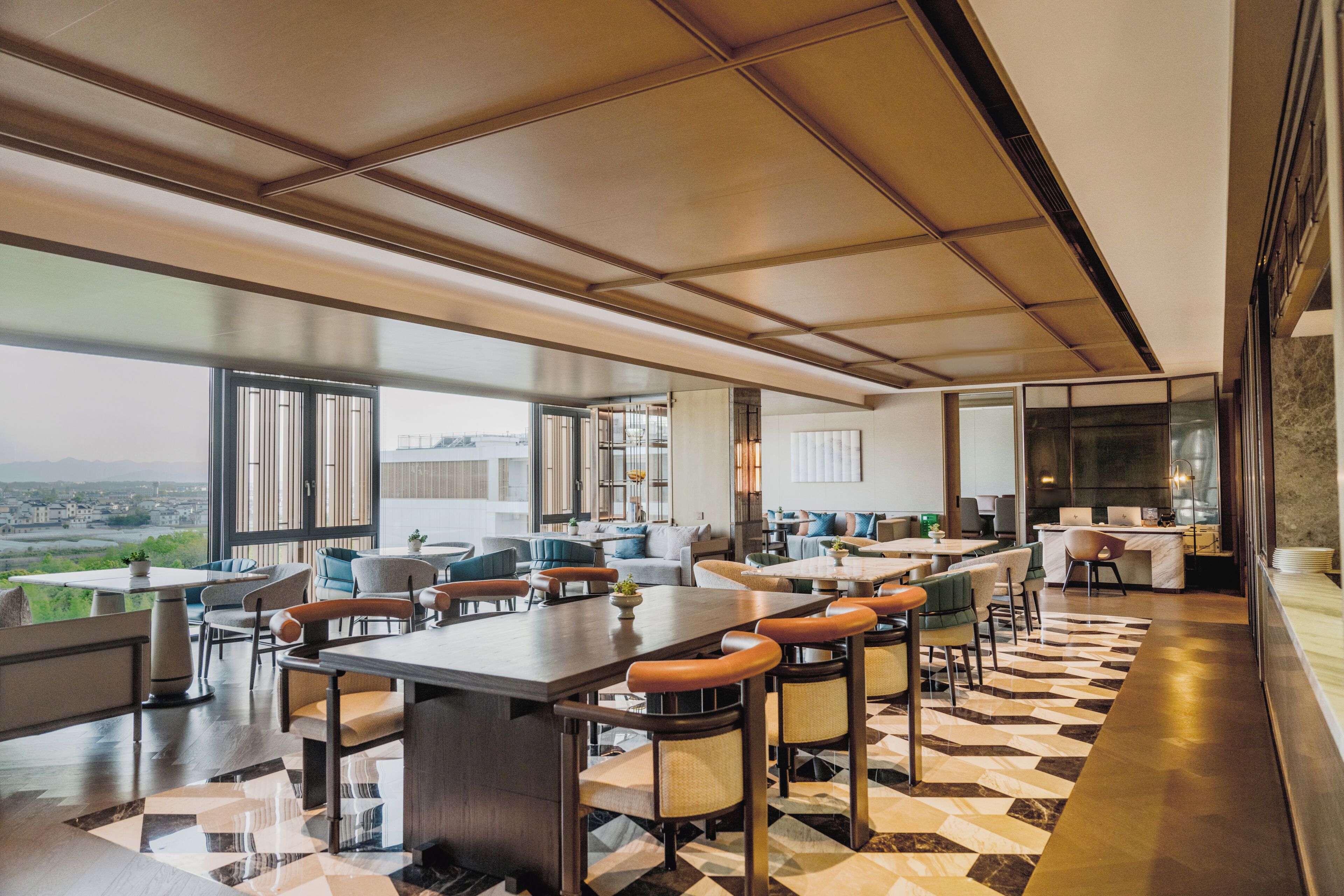 Un interior moderno con un amplio comedor, varias opciones de asientos y grandes ventanas que ofrecen vistas a la ciudad.