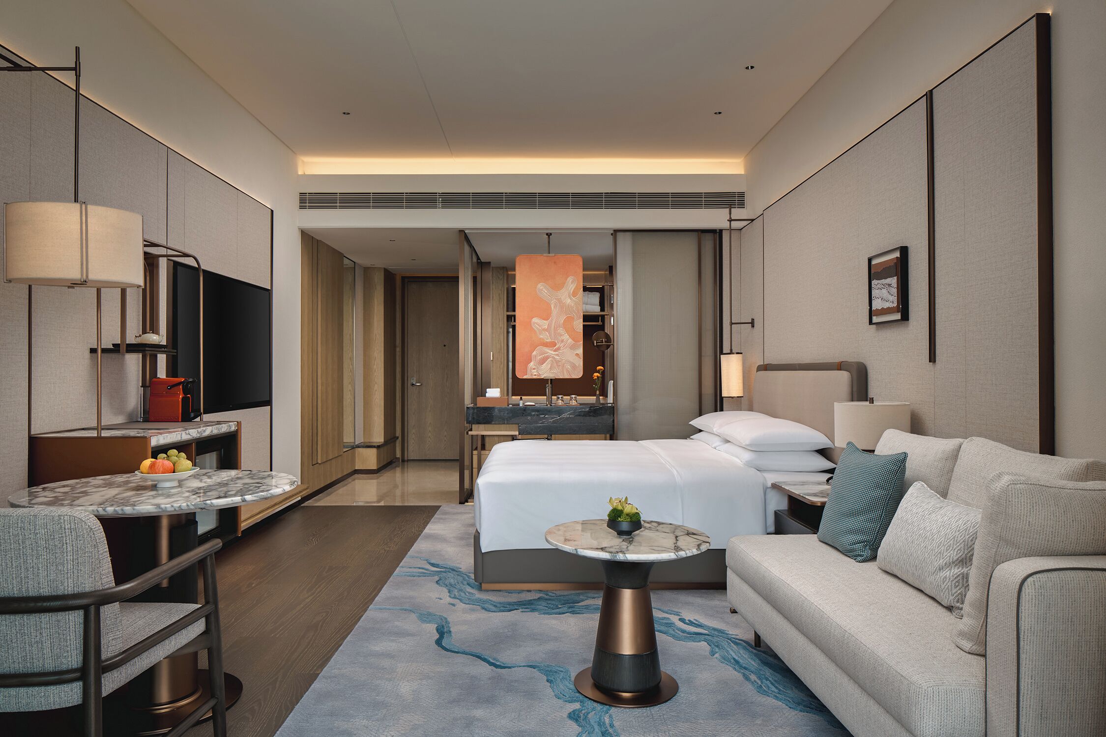 Habitación de hotel moderna con cama, sofá, una mesita, televisor y escritorio con silla.