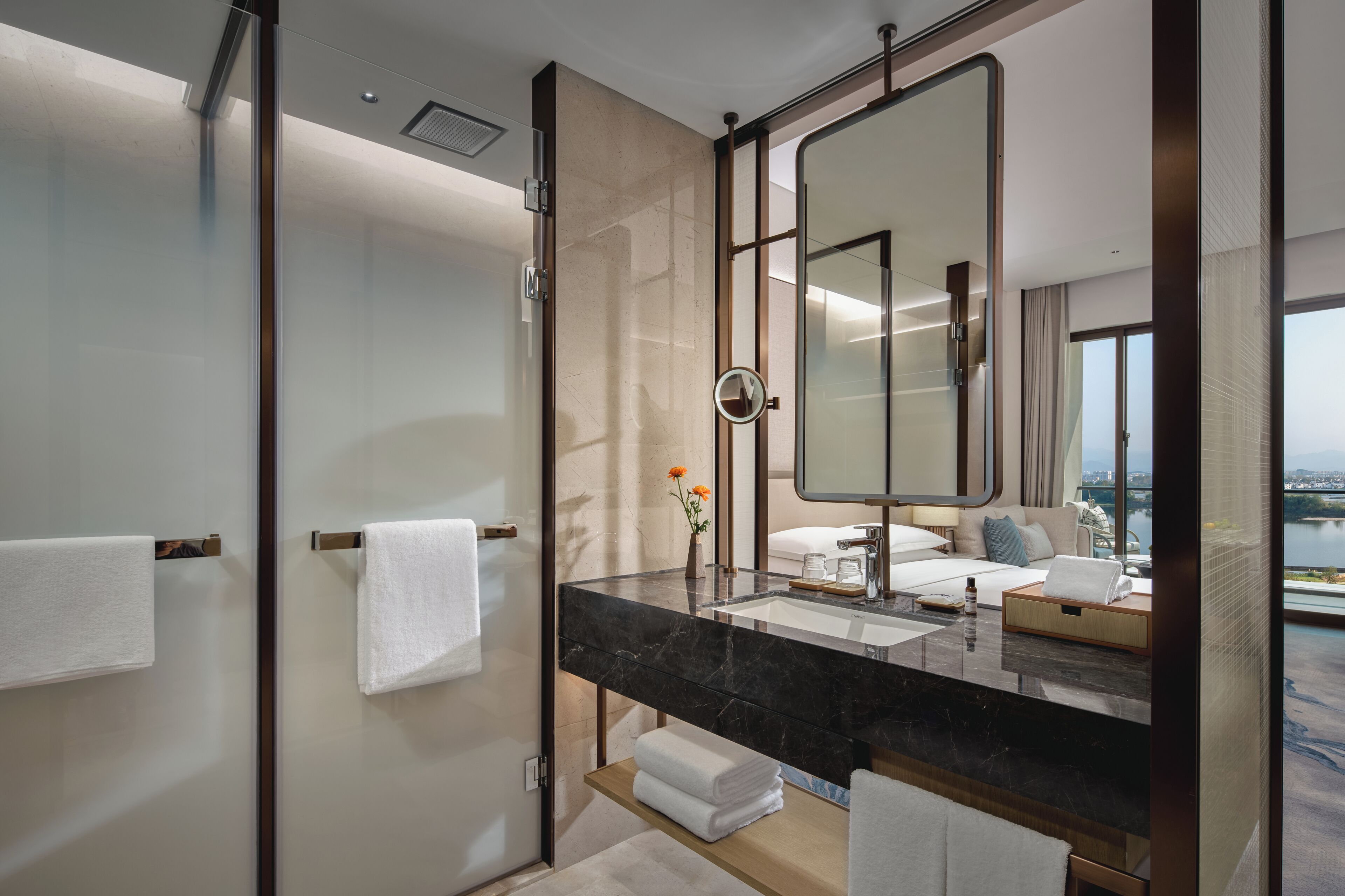 A modern bathroom with a large mirror, a black marble countertop, and a view of a cityscape through large windows.