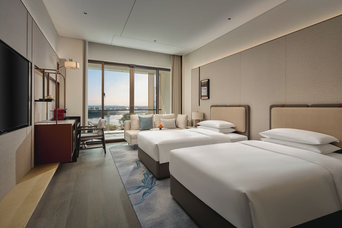 Une chambre d’hôtel avec deux lits, un bureau, une télévision et une grande fenêtre donnant sur la ville.