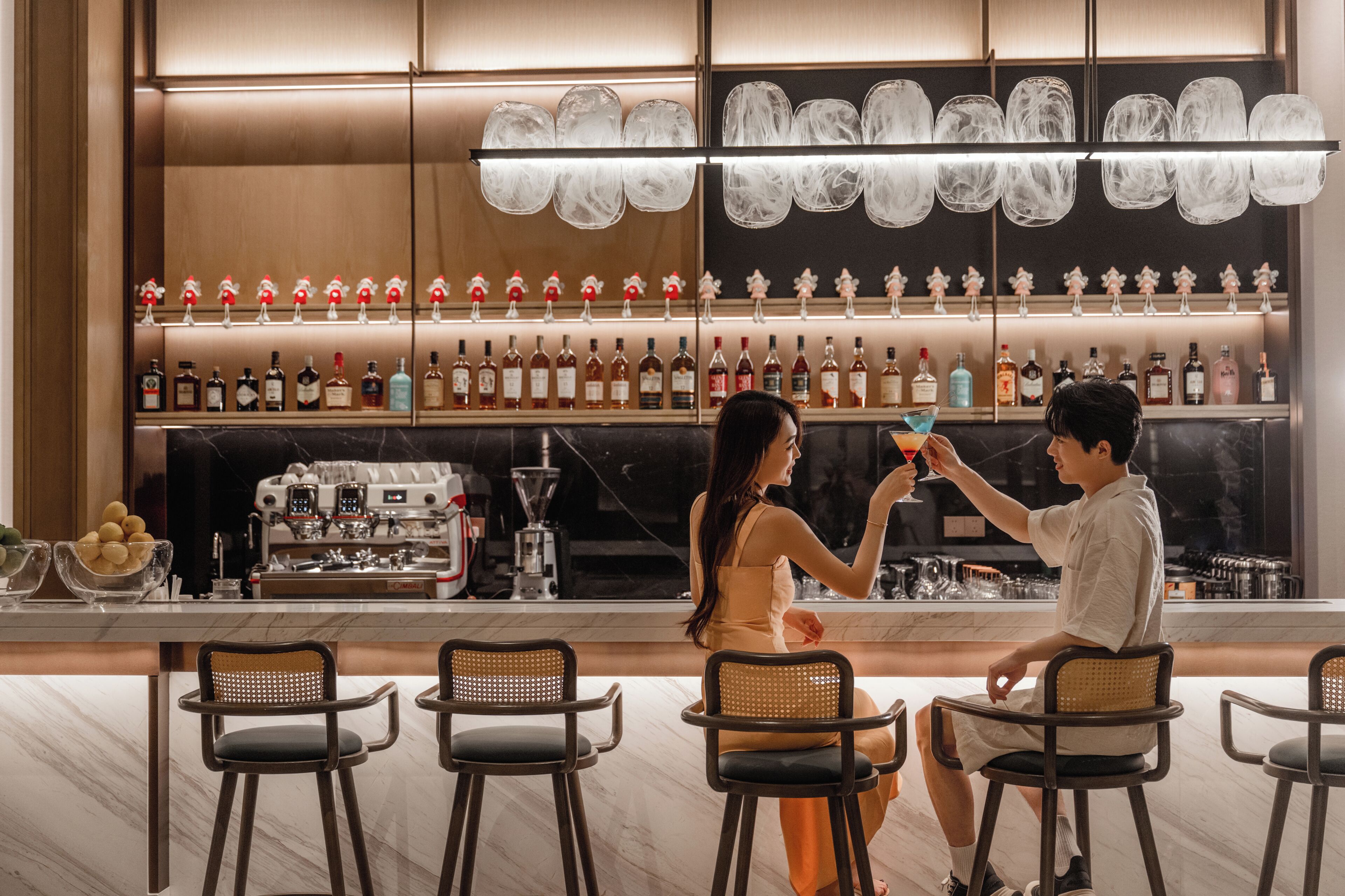 A bar area with multiple seating arrangements and a variety of bottles on shelves.